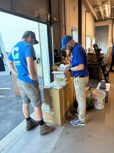 Two Cape Heating technicians in blue uniforms unboxing a new Daikin HVAC unit inside the company's Cape Cod, MA warehouse