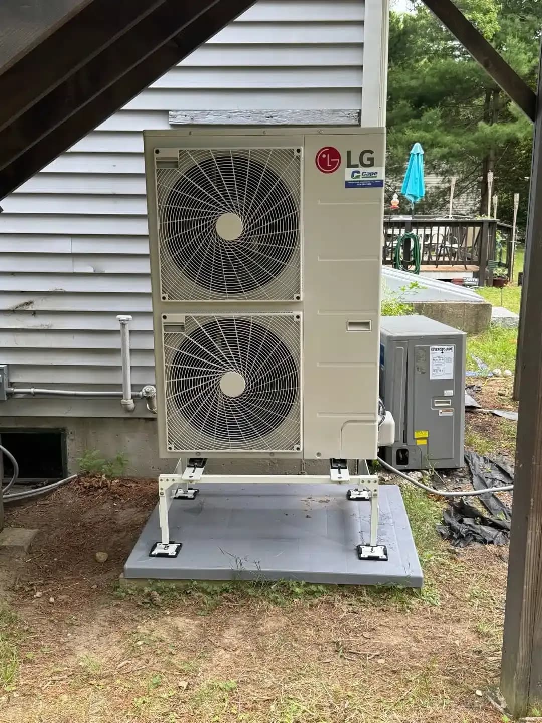 LG outdoor heat pump condenser installed beside a Cape Cod, MA home, bearing a Cape Heating service sticker