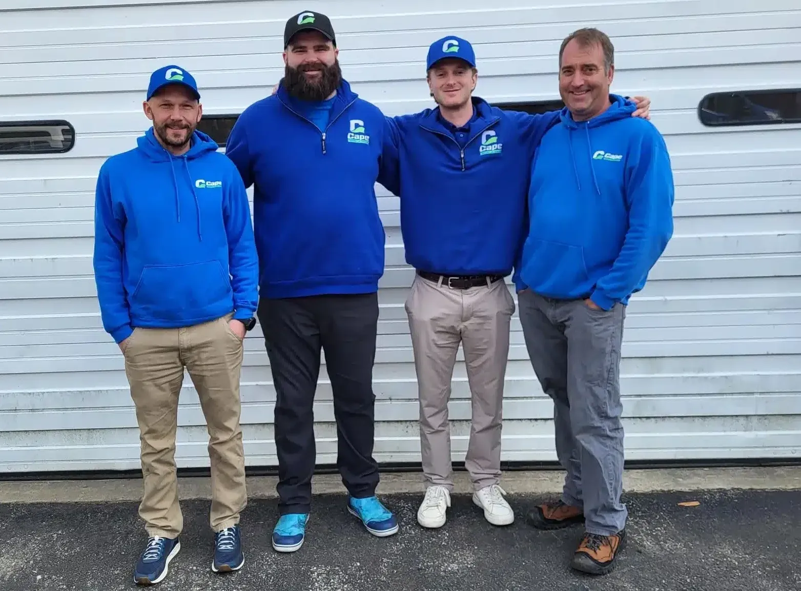 Four Cape Heating AC & Electric technicians in blue branded gear posing outside their Cape Cod, MA shop